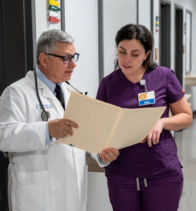 A doctor and a nurse review a chart while standing in a hallway.