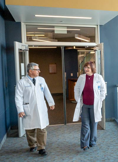 Two physicians in white coats talk while walking.